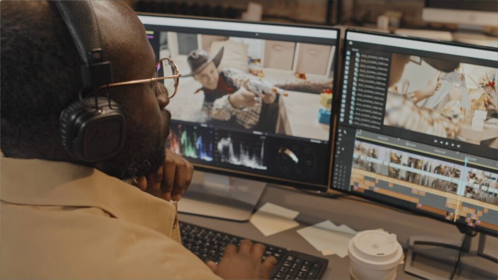 man sitting at desk with headphones two monitors video editing software