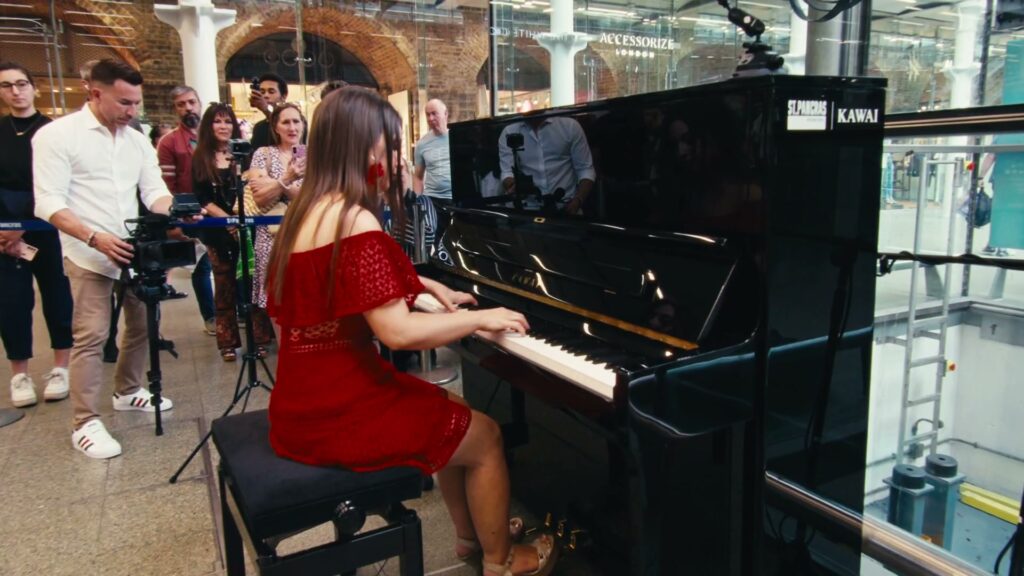 Kawai public piano at St Pancras International A pianist playing the Kawai public piano at St Pancras International, watched by a crowd of passers-by.