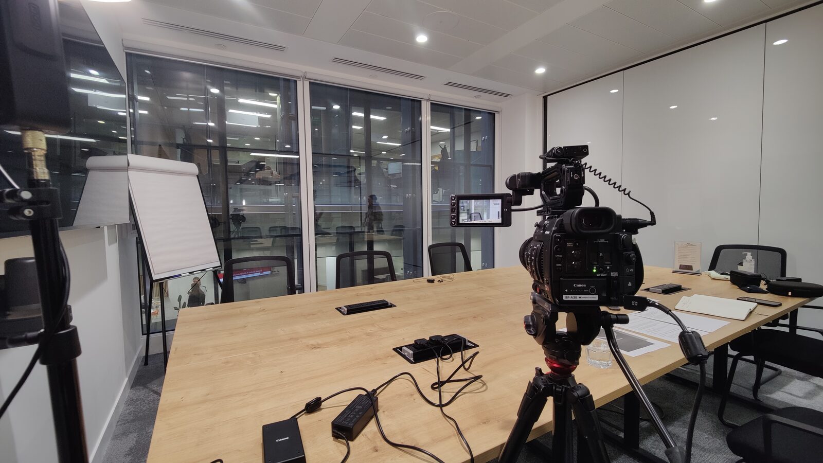 A Lumira Studio camera set up on a tripod beside a laptop in an empty meeting room before a filming day